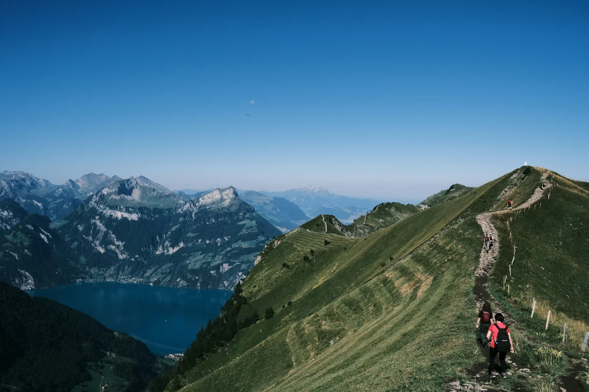 Hikers walking a mountain ridge trail above an alpine lake
